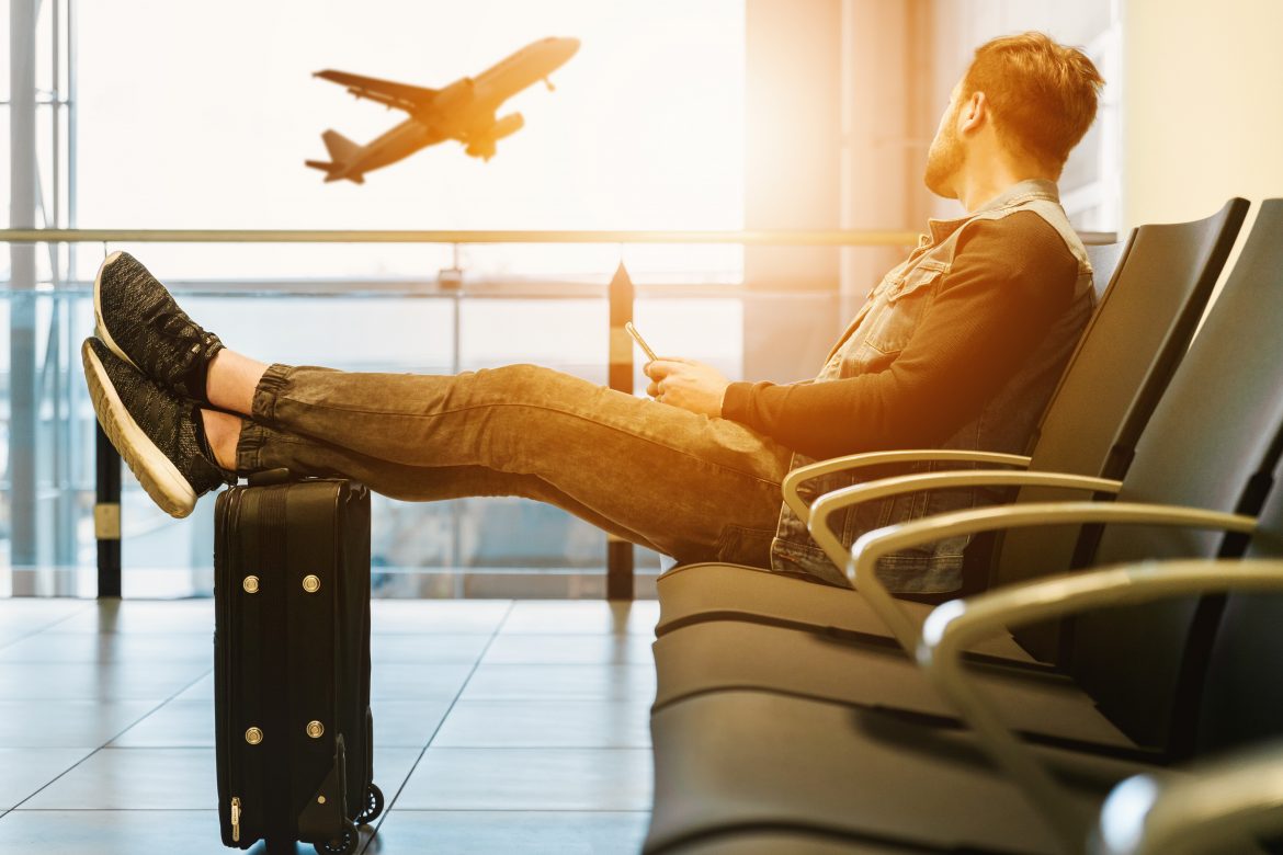 homme assis dans un aéroport avec les pieds sur sa valise regardant les avions décoller